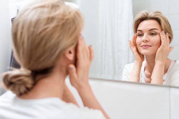 Woman looking the result of her BBL treatment in the mirror at Kingsway Dermatology